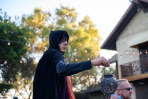 A person in a mask, cloak, and hood, holding a lantern