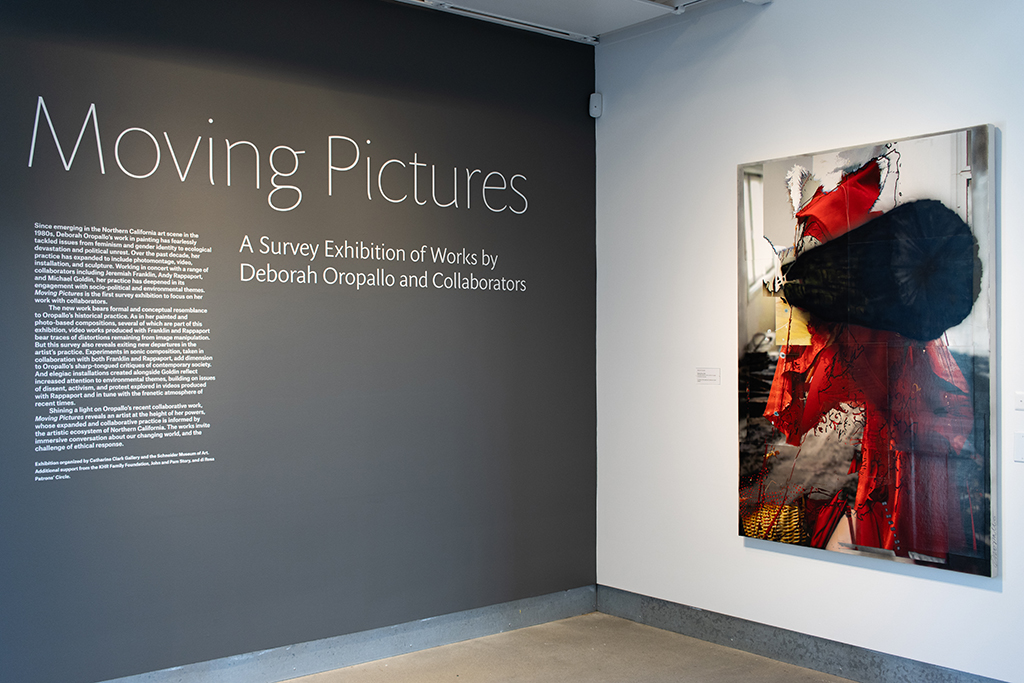 A wall with text reading "Moving Pictures," facing a wall with a large painting of a fragmented figure.