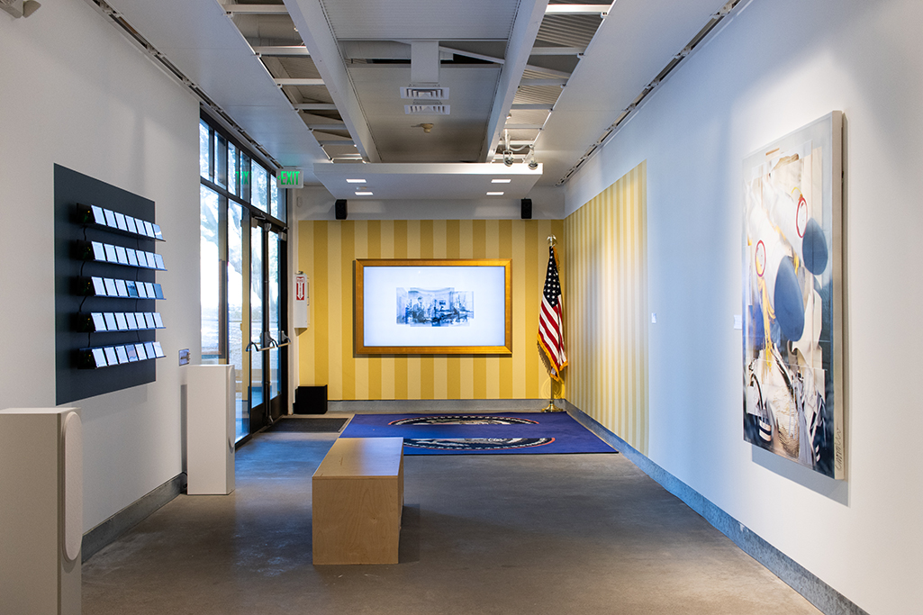 A gallery hallway with various works, the end painted like the oval office