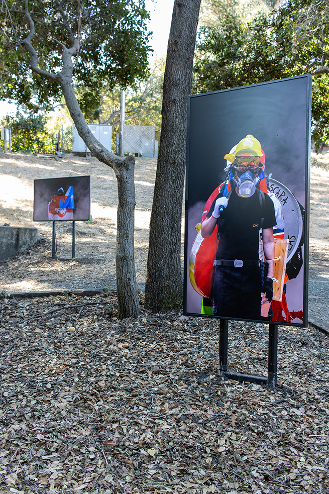 A video monitor in a grove of trees with an image of a masked protestor