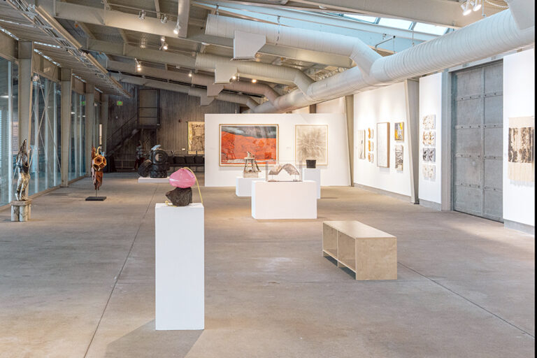 An assortment of artworks, including paintings, drawings, and sculpture, in a gallery.