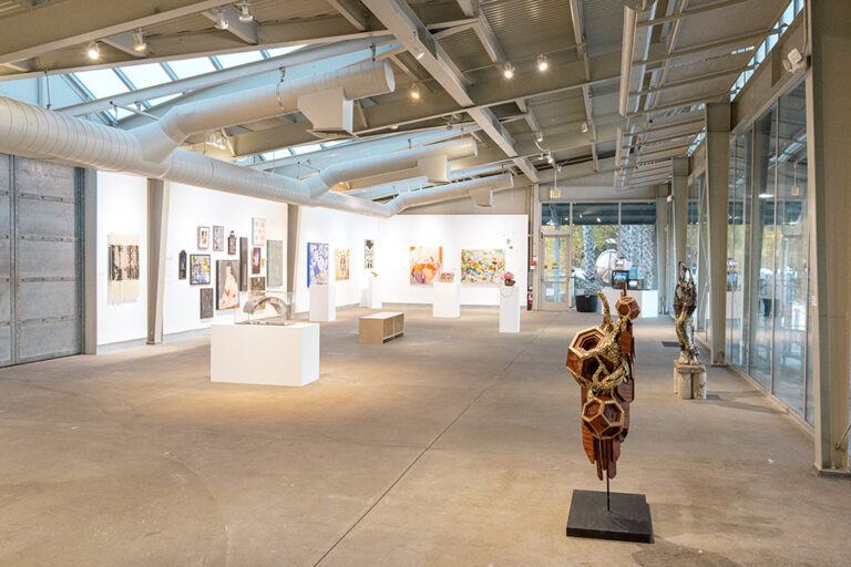 An assortment of artworks, including paintings, drawings, and sculpture, in a gallery.